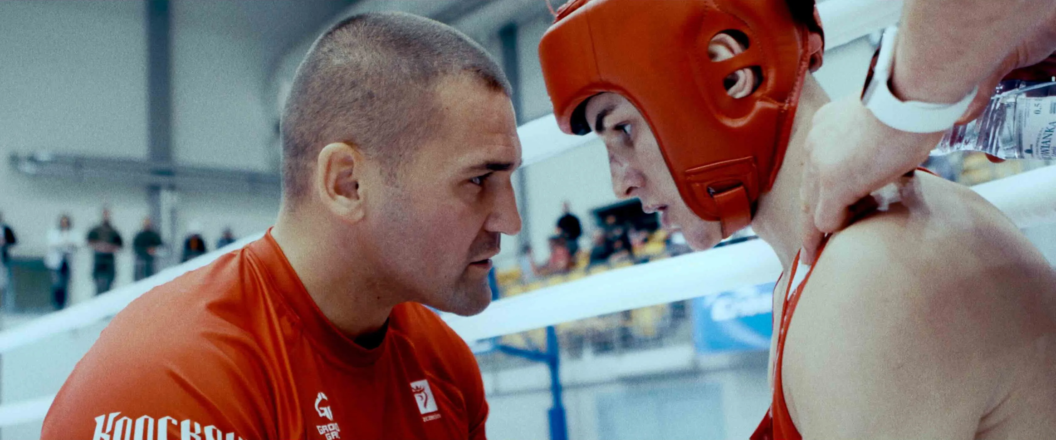 A coach speaks to a young boxer in red headgear between rounds