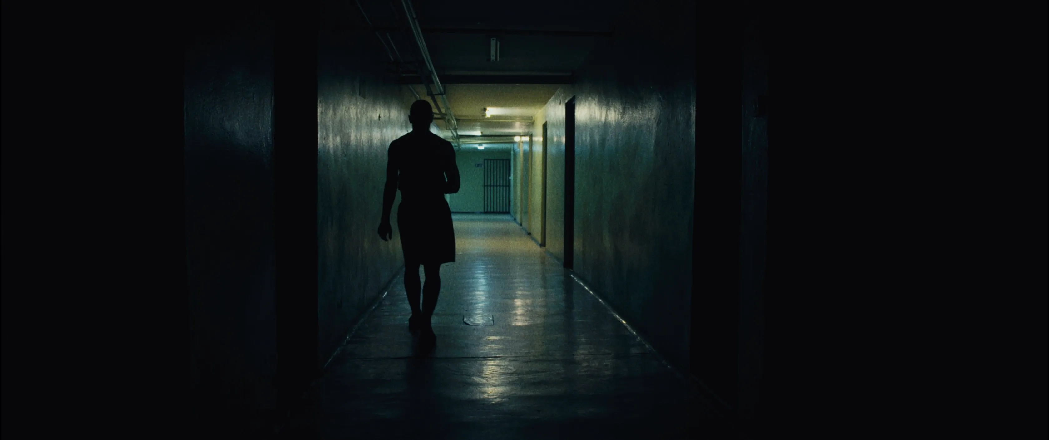 Silhouette of a young boxer walking down a long, dark corridor