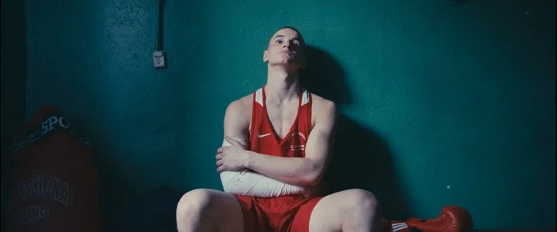 A young boxer in a red vest sits against a teal wall, head tilted back
