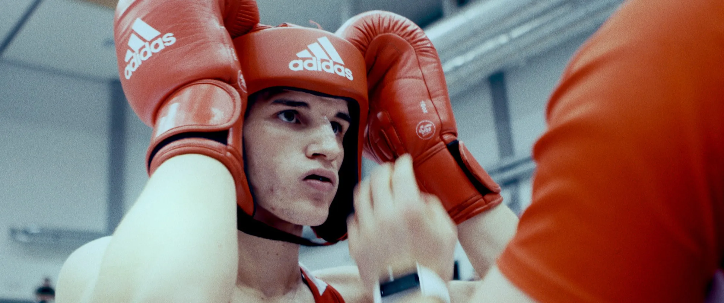 Łukasz Perkowski in red headgear and boxing gloves as his coach adjusts the headgear
