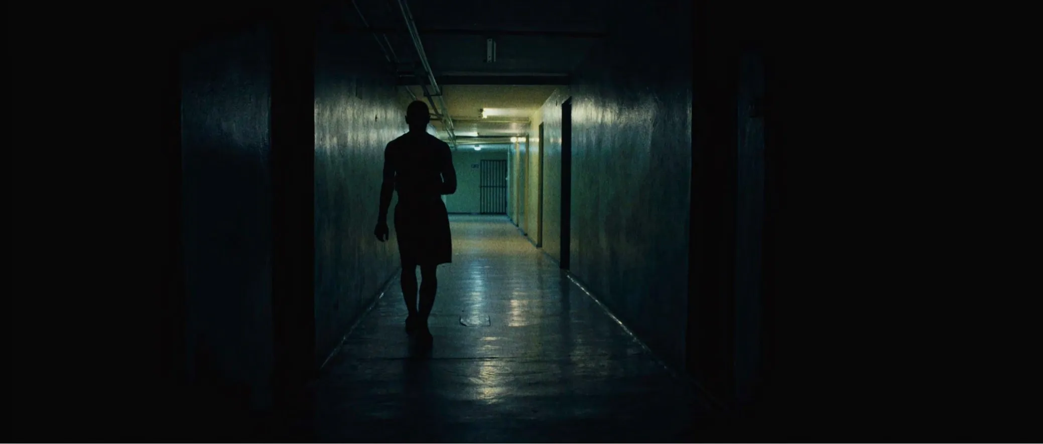 Silhouette of a young boxer walking down a long, dark corridor
