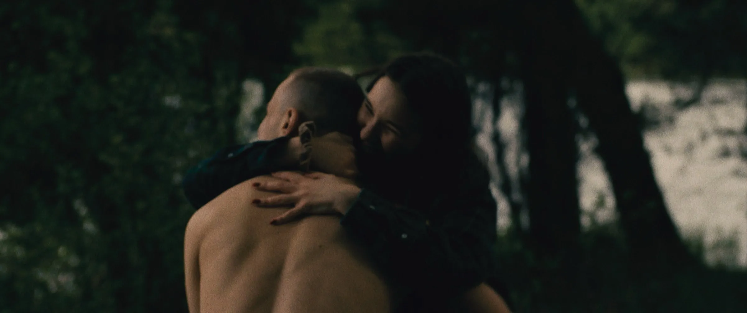 Olimpia embraces Łukasz at dusk under the trees
